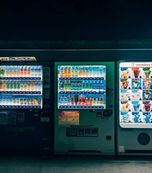Row of commercial beverage vending machines placed outdoors along a roadside, fully stocked with cold drinks
